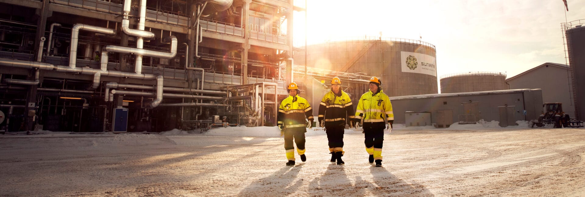 Three workers in protective clothing in front of industrial building.
