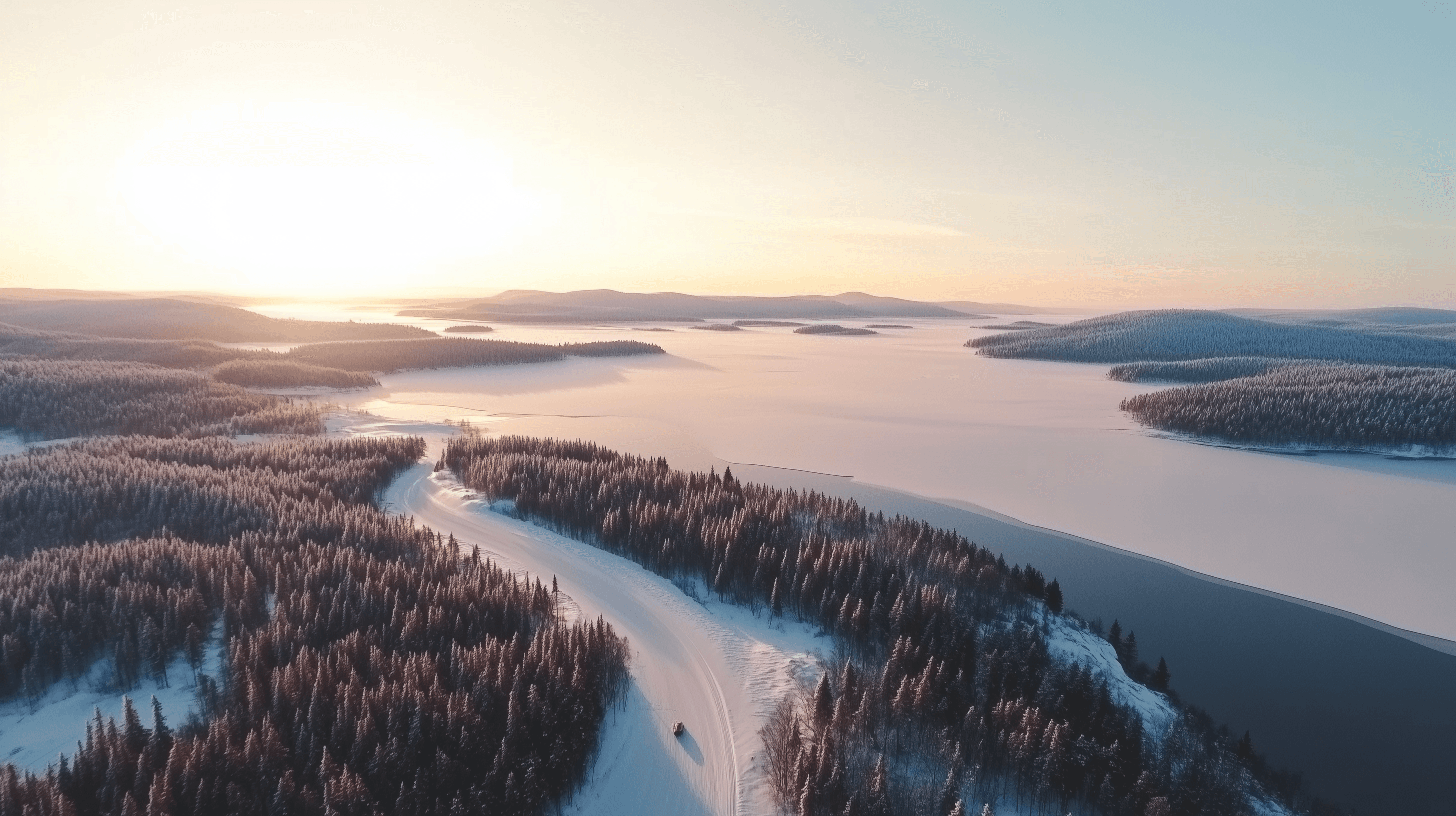 Snötäckt landskap med solnedgång över skog och sjö.
