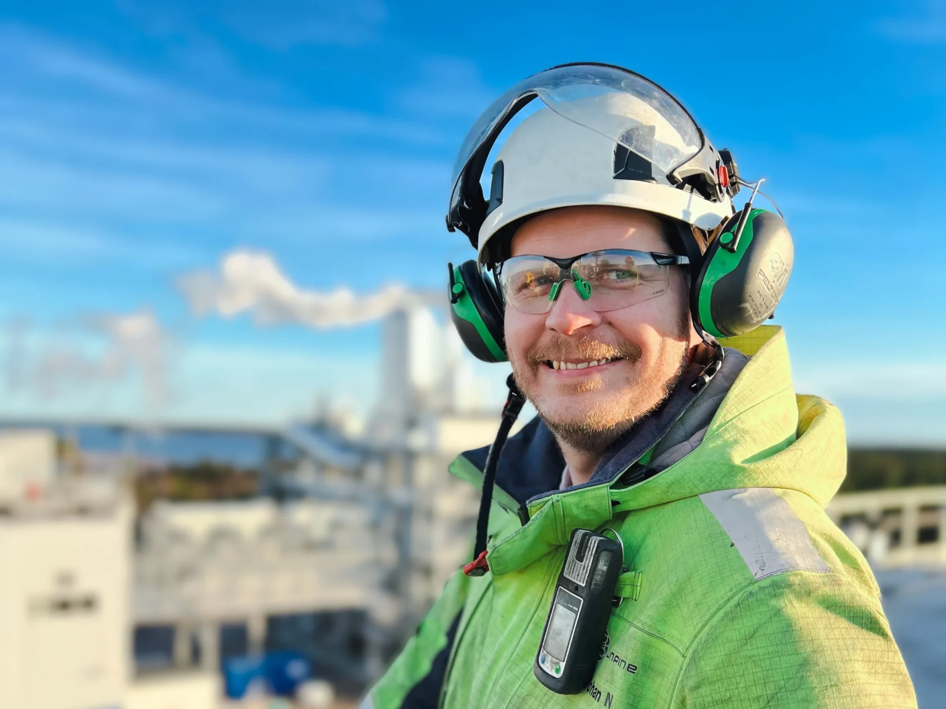 Smiling worker with helmet and goggles outdoors.